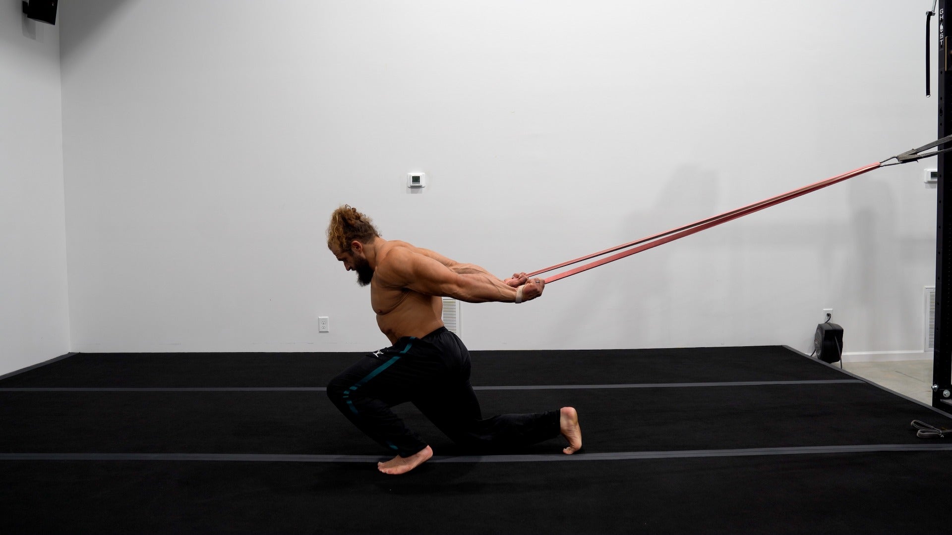 Man exercising with resistance bands in a room with white walls and black floor.