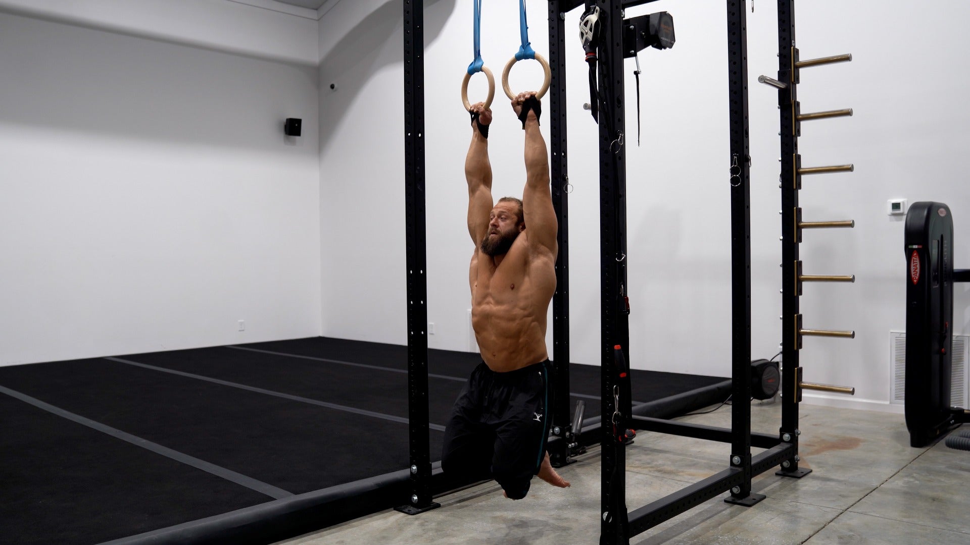 Man performing a pull-up on gymnastic rings in a home gym.