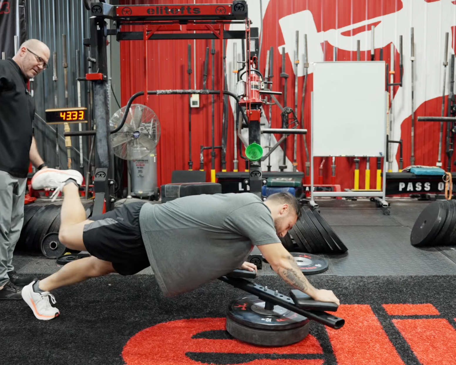 Person performing push-ups with weights on a gym floor, surrounded by gym equipment.
